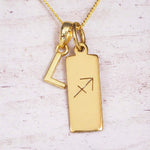Gold Sagittarius initial necklace with a letter L charm and engraved zodiac bar on white wood, close-up