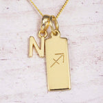 Gold Sagittarius initial necklace with a letter N charm and engraved zodiac bar on white wood, close-up