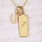 Gold Sagittarius initial necklace with a letter U charm and engraved zodiac bar on white wood, close-up