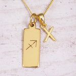Gold Sagittarius initial necklace with a letter X charm and engraved zodiac bar on white wood, close-up