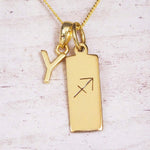 Gold Sagittarius initial necklace with a letter Y charm and engraved zodiac bar on white wood, close-up