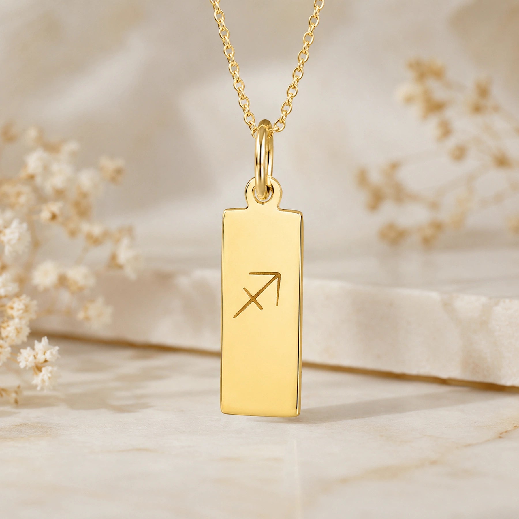 gold sagittarius necklace featuring rectangle pendant engraved with minimalist sagittarius zodiac star sign line glyph symbol suspended from a fine chain