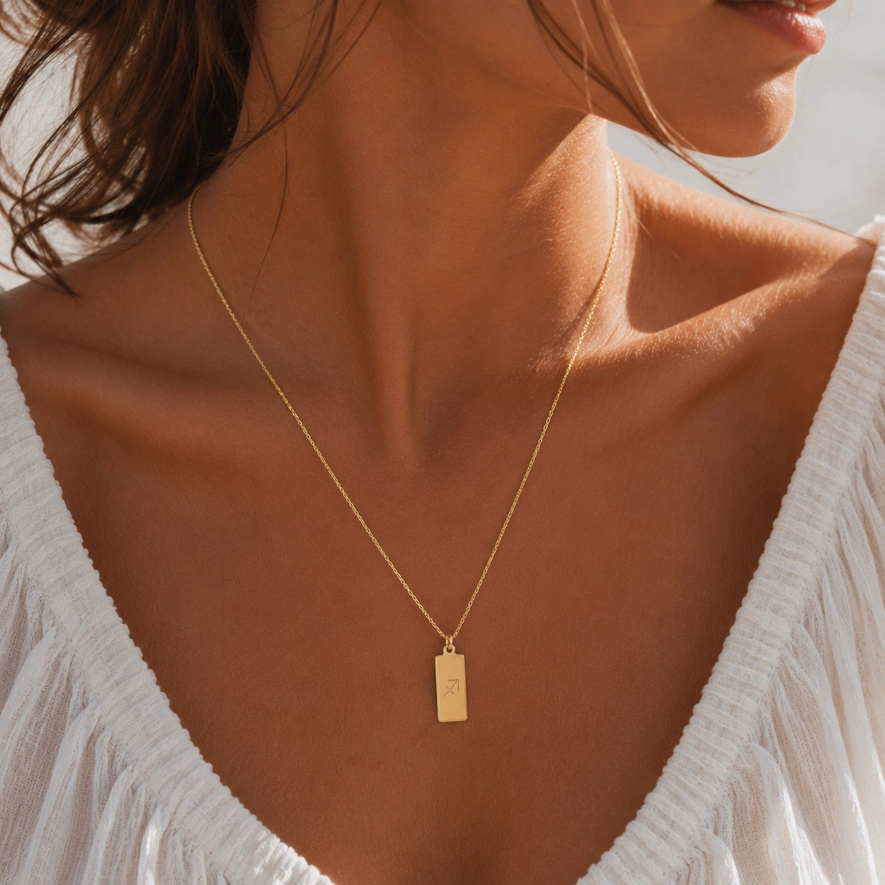model wearing a dainty gold fine chain necklace with a rectangle pendant engraved with sagittarius zodiac line glyph symbol.
