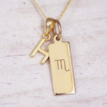 Gold Scorpio initial necklace with a letter H charm and engraved zodiac bar on white wood, close-up