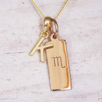 Gold Scorpio initial necklace with a letter K charm and engraved zodiac bar on white wood, close-up