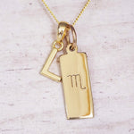 Gold Scorpio initial necklace with a letter L charm and engraved zodiac bar on white wood, close-up
