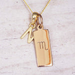 Gold Scorpio initial necklace with a letter N charm and engraved zodiac bar on white wood, close-up