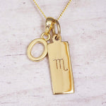 Gold Scorpio initial necklace with a letter O charm and engraved zodiac bar on white wood, close-up