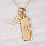 Gold Scorpio initial necklace with a letter P charm and engraved zodiac bar on white wood, close-up