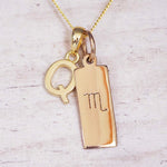 Gold Scorpio initial necklace with a letter Q charm and engraved zodiac bar on white wood, close-up