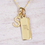 Gold Scorpio initial necklace with a letter S charm and engraved zodiac bar on white wood, close-up