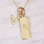Gold Scorpio initial necklace with a letter V charm and engraved zodiac bar on white wood, close-up