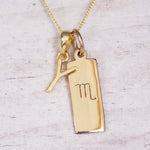 Gold Scorpio initial necklace with a letter Y charm and engraved zodiac bar on white wood, close-up