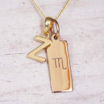 Gold Scorpio initial necklace with a letter Z charm and engraved zodiac bar on white wood, close-up