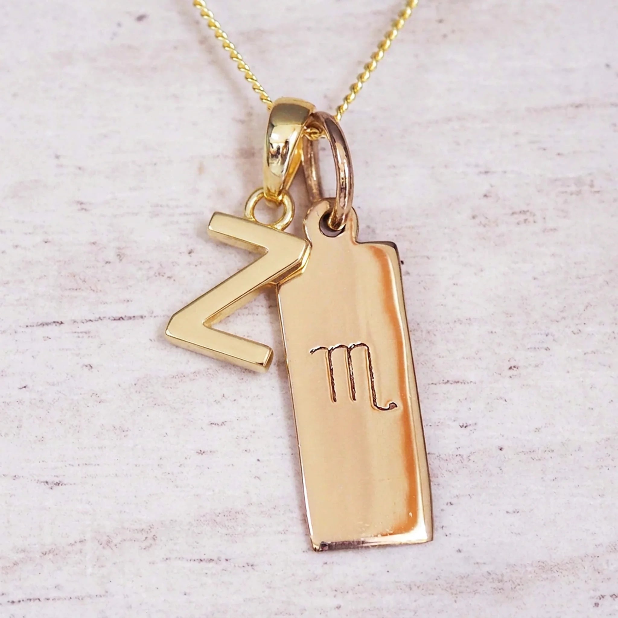 Gold Scorpio initial necklace with a letter Z charm and engraved zodiac bar on white wood, close-up
