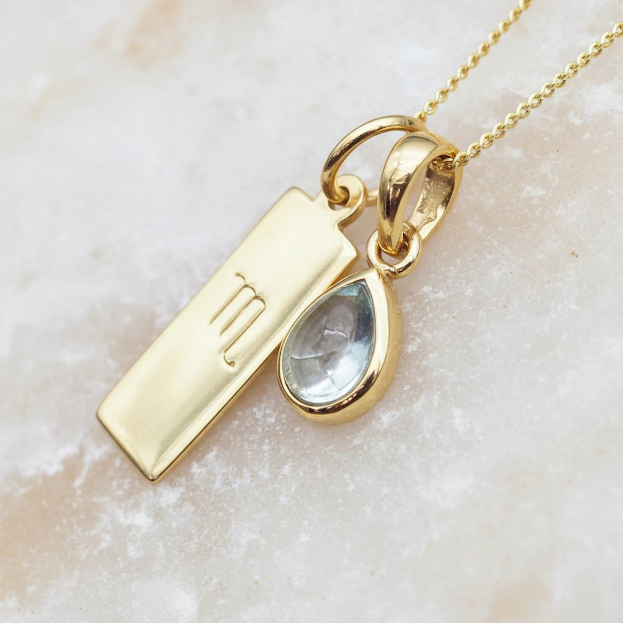 Gold necklace with Scorpio zodiac pendant and November birthstone topaz gemstone pendant on a light background