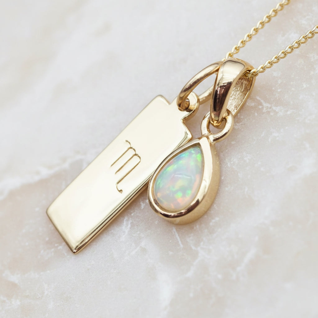 Gold necklace with a Scorpio symbol pendant and opal stone on a warm stone background
