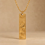 Gold Scorpio zodiac necklace, embossed bar pendant with sign symbol on a faceted ball chain, warm beige background
