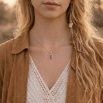 Close-up of a person wearing a gold necklace with a blue pendant, outdoors.