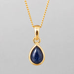 september birthstone natural sapphire necklace - A gold teardrop pendant necklace featuring a deep blue cabochon gemstone, suspended from a delicate gold chain against a neutral gray background.