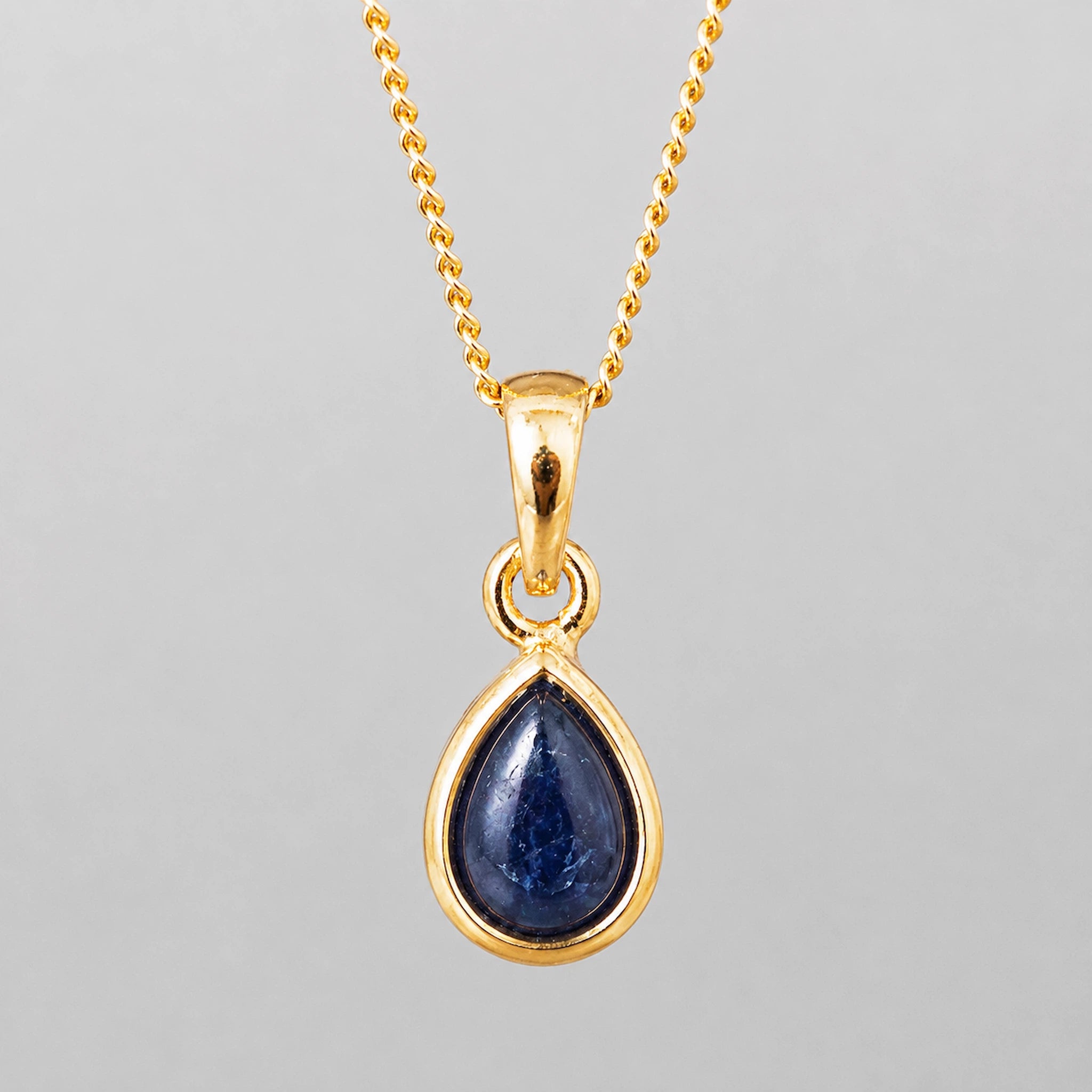 september birthstone natural sapphire necklace - A gold teardrop pendant necklace featuring a deep blue cabochon gemstone, suspended from a delicate gold chain against a neutral gray background.