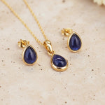 Gold necklace and earrings with september birthstone blue teardrop sapphire stones on a beige surface