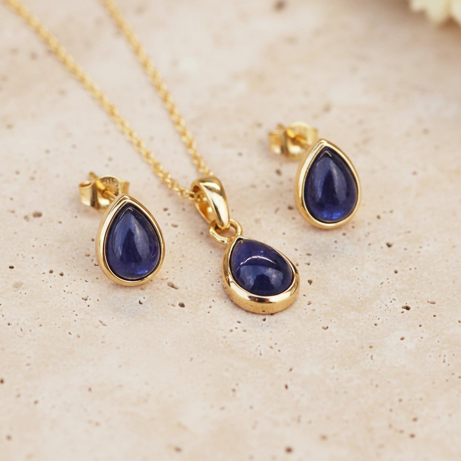Gold necklace and earrings with september birthstone blue teardrop sapphire stones on a beige surface