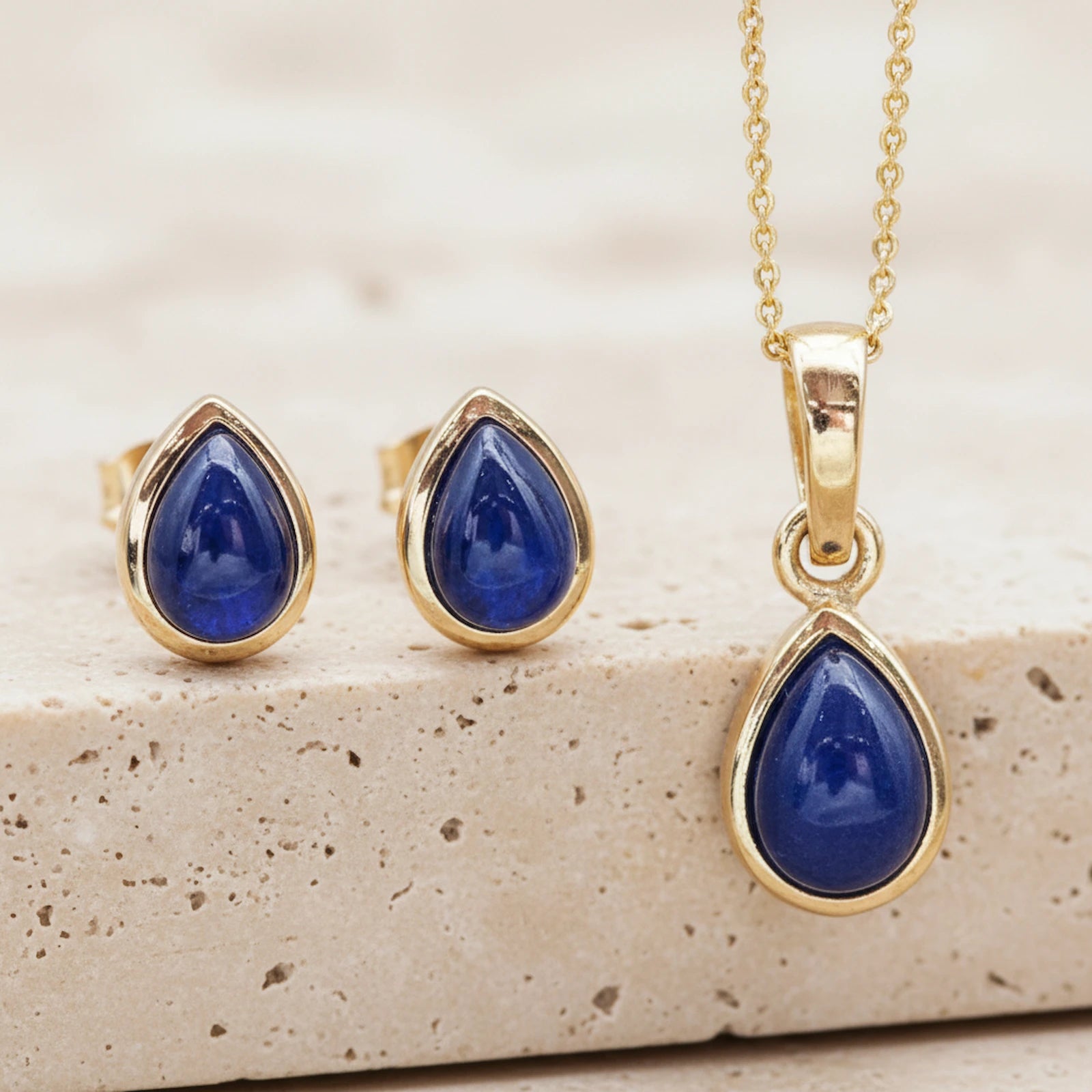 Gold jewellery set with september birthstone blue sapphire stones on a stone surface