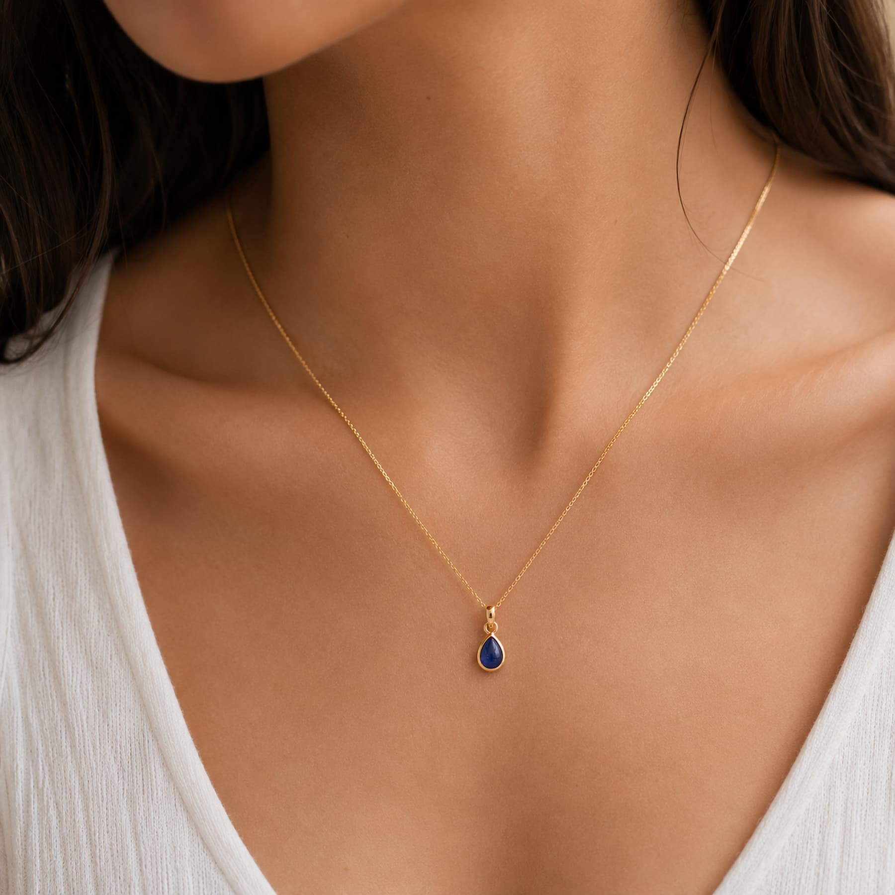 close up of model wearing a dainty gold september birthstone natural sapphire teardrop pendant necklace