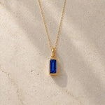 Gold fine chain necklace with a rectangle faceted bezel set september cubic zirconia pendant on a light stone background.