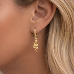 Gold snake-shaped earring worn by a person with blonde hair.