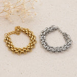 Gold and silver chunky chain bracelets on a textured beige surface with dried flowers. waterproof jewellery