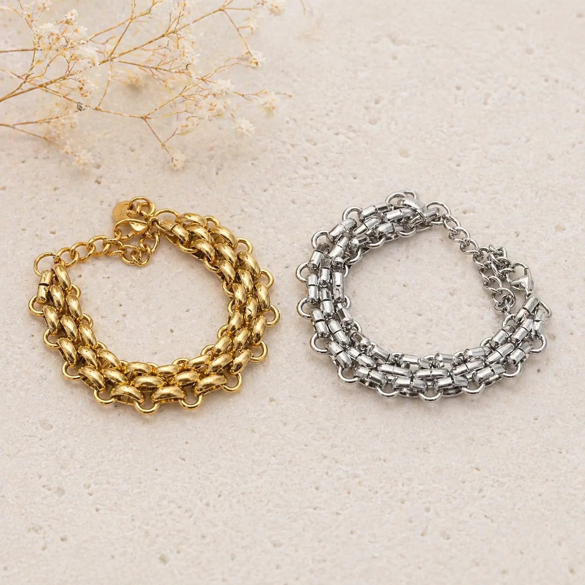 Gold and silver chunky chain bracelets on a textured beige surface with dried flowers. waterproof jewellery