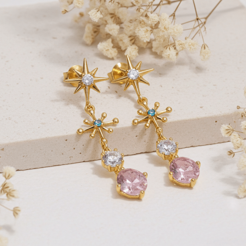 Gold earrings with pink gemstones on a light background with dried flowers.