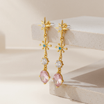 Gold earrings with pink gemstones on a beige surface
