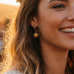 Woman wearing gold earrings and necklace with a blurred background