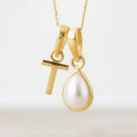 Gold necklace with a 'T' pendant and a teardrop-shaped pearl on a light background