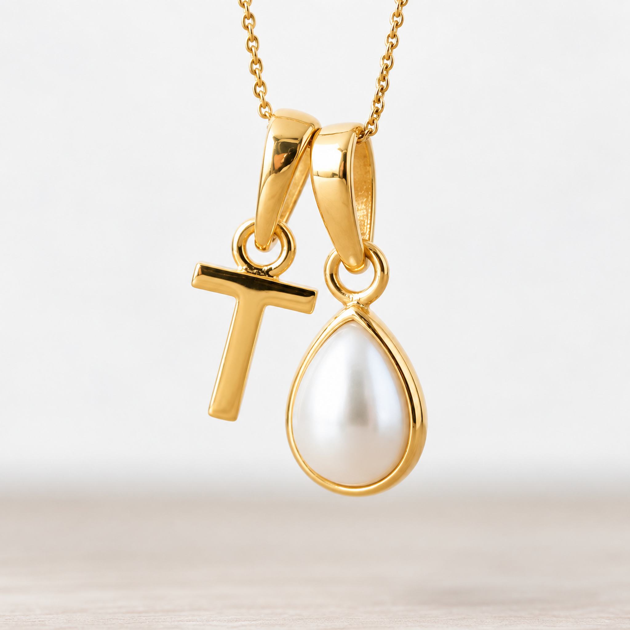 Gold June birthstone necklace with a pear-shaped natural mother of pearl pendant and letter 'T' charm.