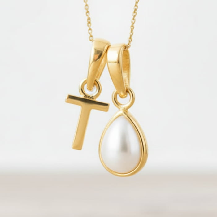 Gold necklace with a 'T' pendant and a teardrop-shaped pearl on a light background