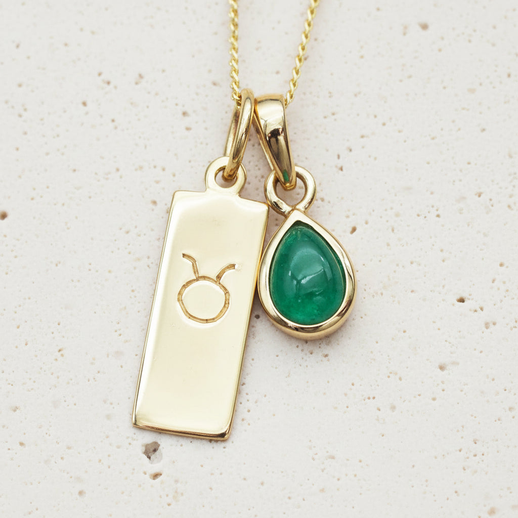 Gold necklace with Taurus zodiac sign pendant and green natural emerald teardrop pendant on a natural background