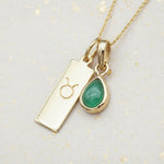 Gold necklace with a May birthstone emerald pendant and a taurus zodiac pendant on a light grey background