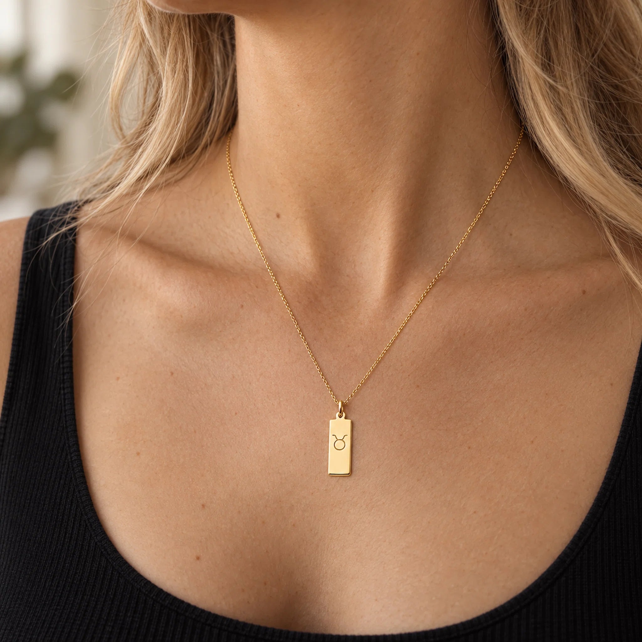 gold taurus necklace worn by a woman, featuring a rectangle pendant engraved with taurus star sign line glyph symbol