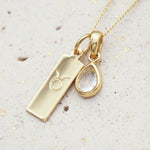 Gold necklace with april birthstone herkimer quartz pendant and Taurus zodiac pendant on a textured beige surface
