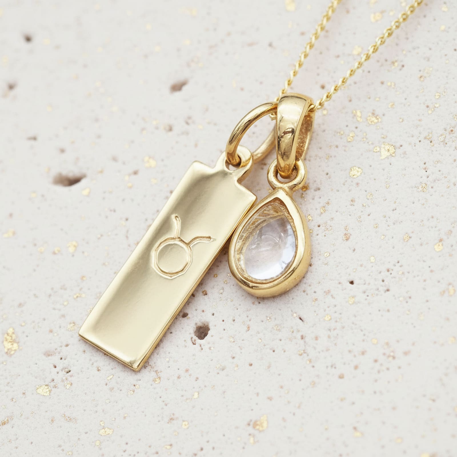 Gold necklace with april birthstone herkimer quartz pendant and Taurus zodiac pendant on a textured beige surface