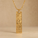 Gold Taurus zodiac necklace, embossed bar pendant with sign symbol on a faceted ball chain, warm beige background