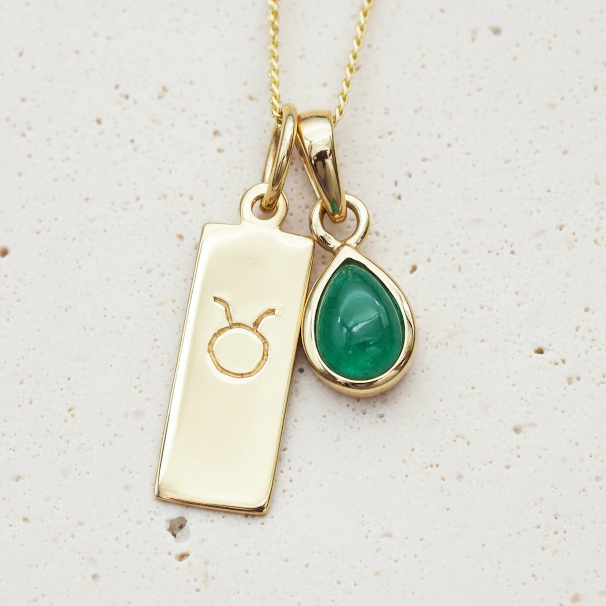 Gold taurus zodiac necklace with a green teardrop-shaped may birthstone emerald gemstone on a light background