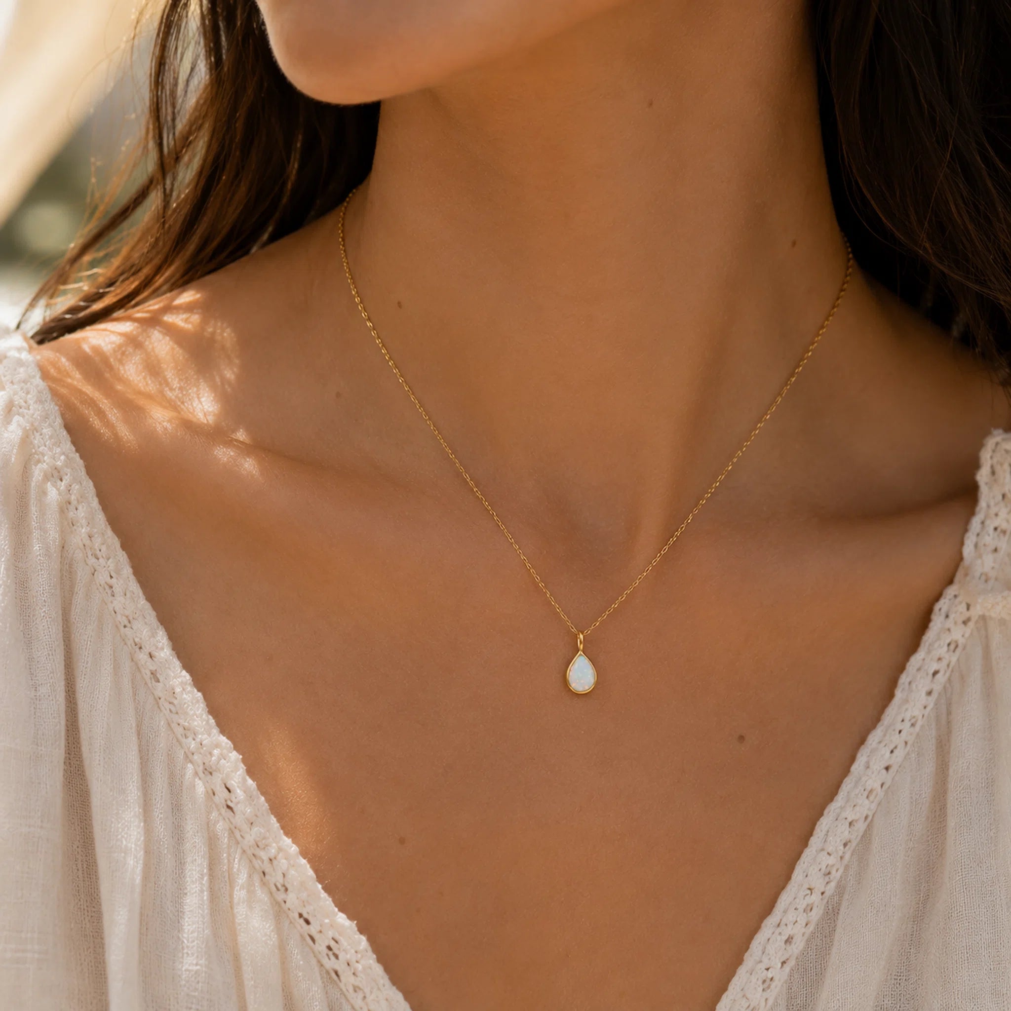 dainty gold necklace with a teardrop white opal being worn