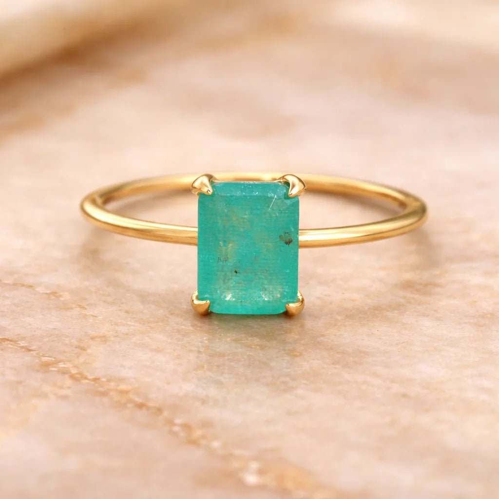Gold ring with a green blue natural tourmaline gemstone on a beige marble background