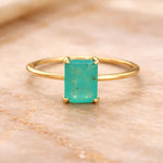 Gold ring with a green blue natural tourmaline gemstone on a beige marble background