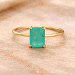 Gold ring with a green blue natural tourmaline gemstone on a beige marble background